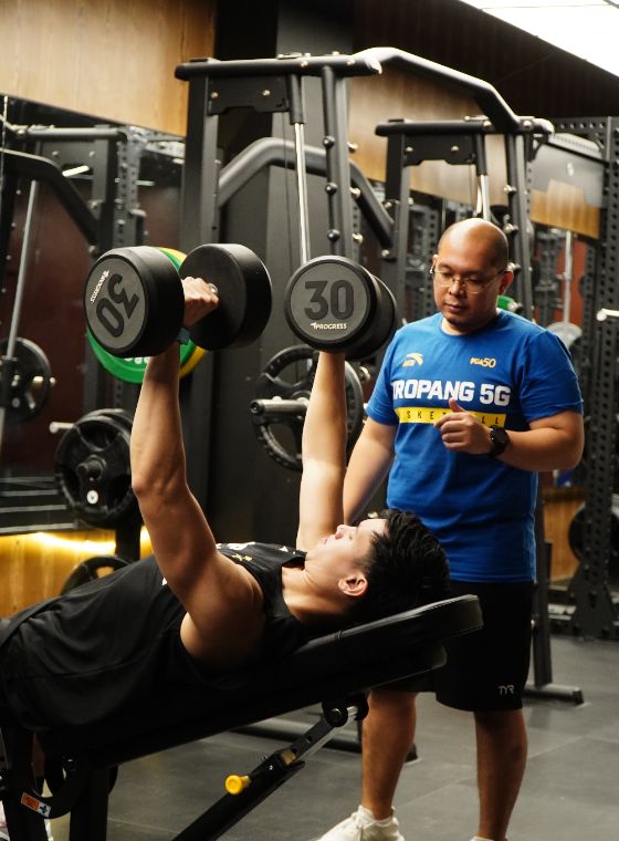 Coach supervising an athlete during a dumbbell press